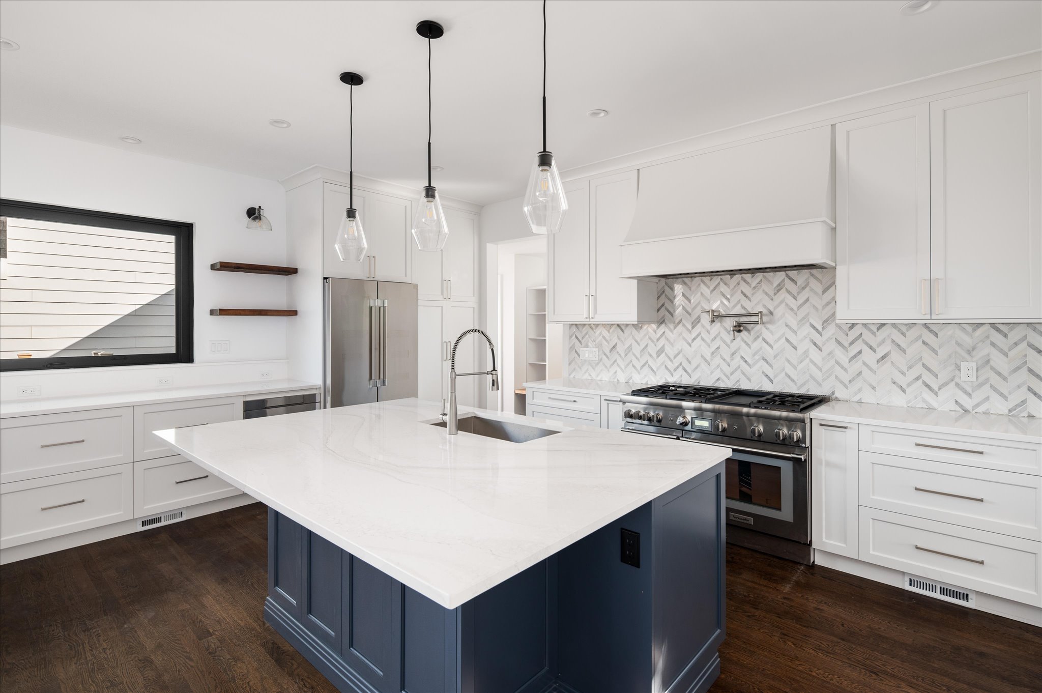 White kitchen cabinetry with a deep blue island and pendant lights.