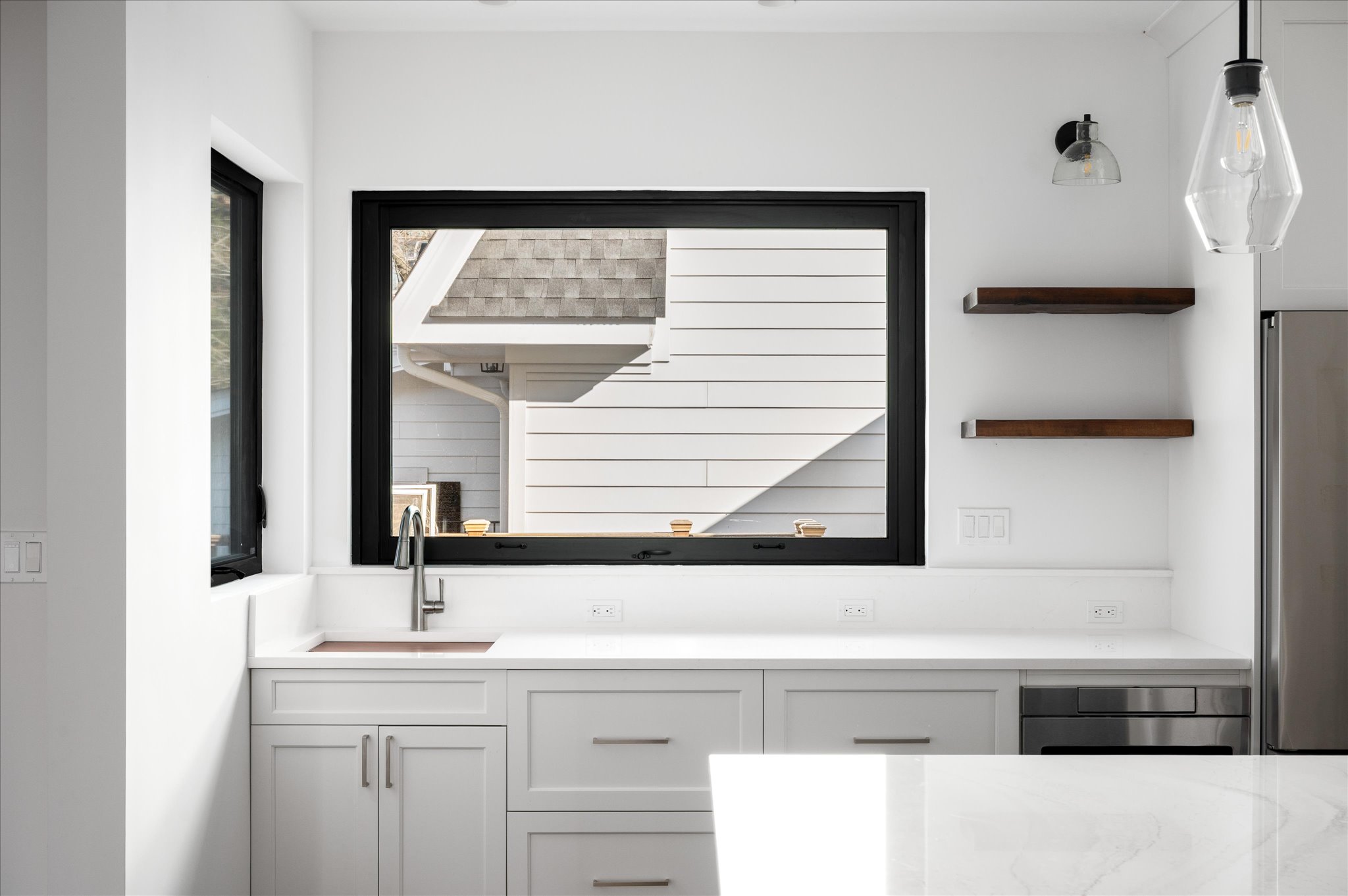 Kitchen sink wall with black-framed window and open shelves.